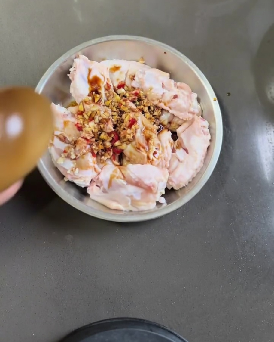 Alitas de pollo crudas en un cuenco metálico mezcladas con ajo, chile, salsa de soja y aceite de sésamo.