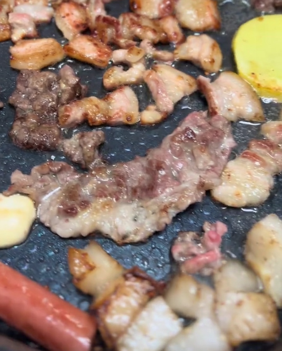 Panceta de cerdo, champiñones y rodajas de patata chisporroteando en una parrilla eléctrica con un dorado apetitoso.