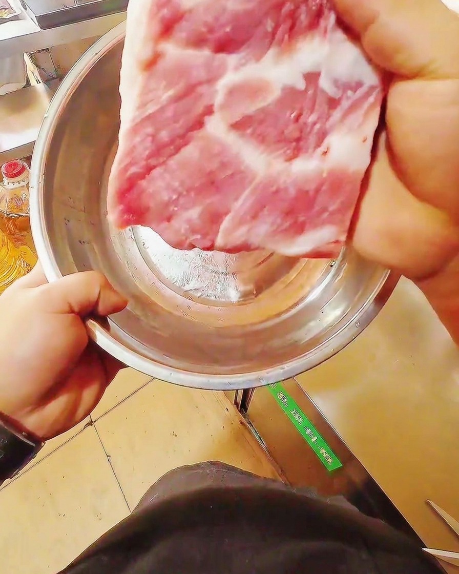 Un cuchillo afilado cortando una tira de panceta de cerdo cruda sobre una tabla de madera.