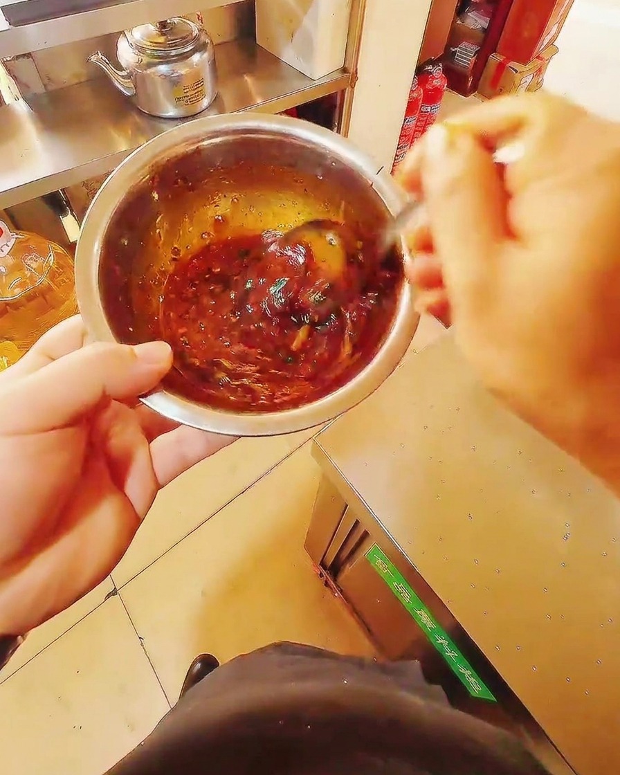 Primer plano de un bol de acero inoxidable con una mezcla de marinado rojo oscuro siendo mezclada con una cuchara de metal.