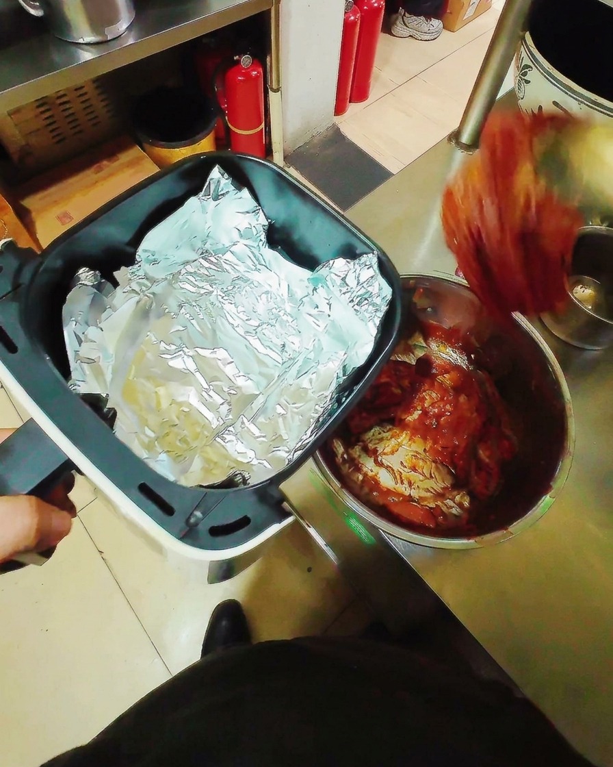 Tiras de cerdo marinado colocadas sobre papel de aluminio dentro de una cesta de freidora de aire.