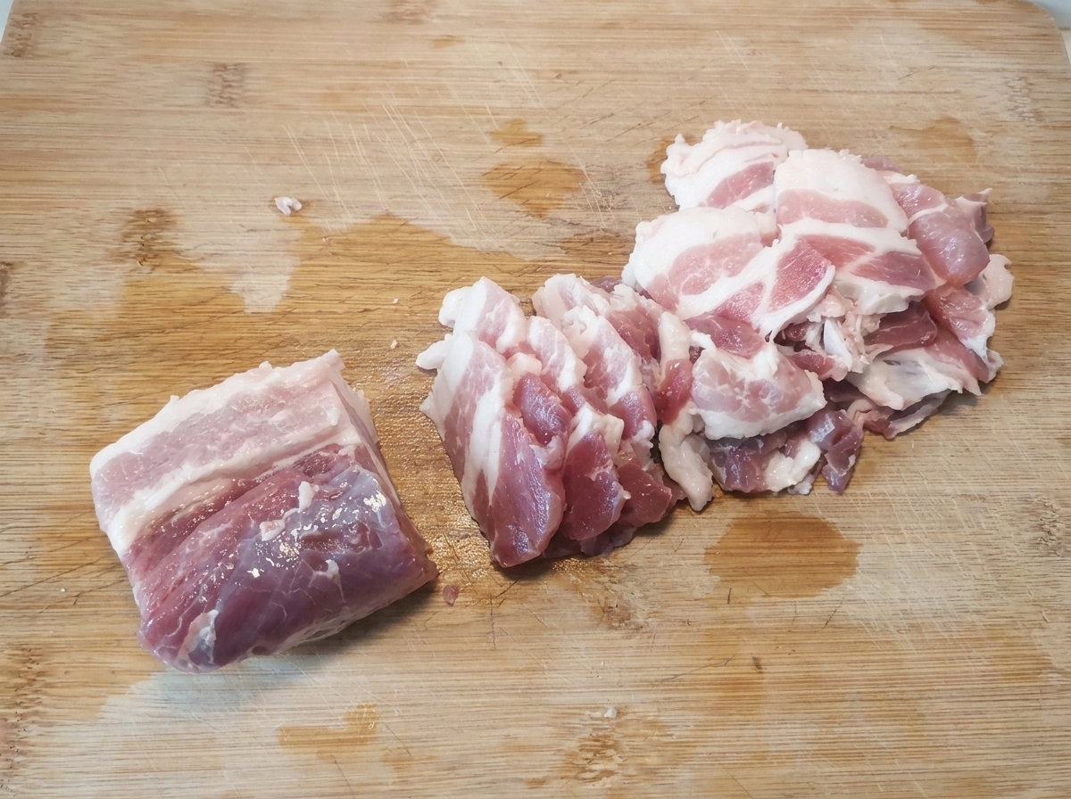 Finas rodajas de panceta de cerdo cruda dispuestas ordenadamente sobre una tabla de cortar de madera después de ser cortadas.