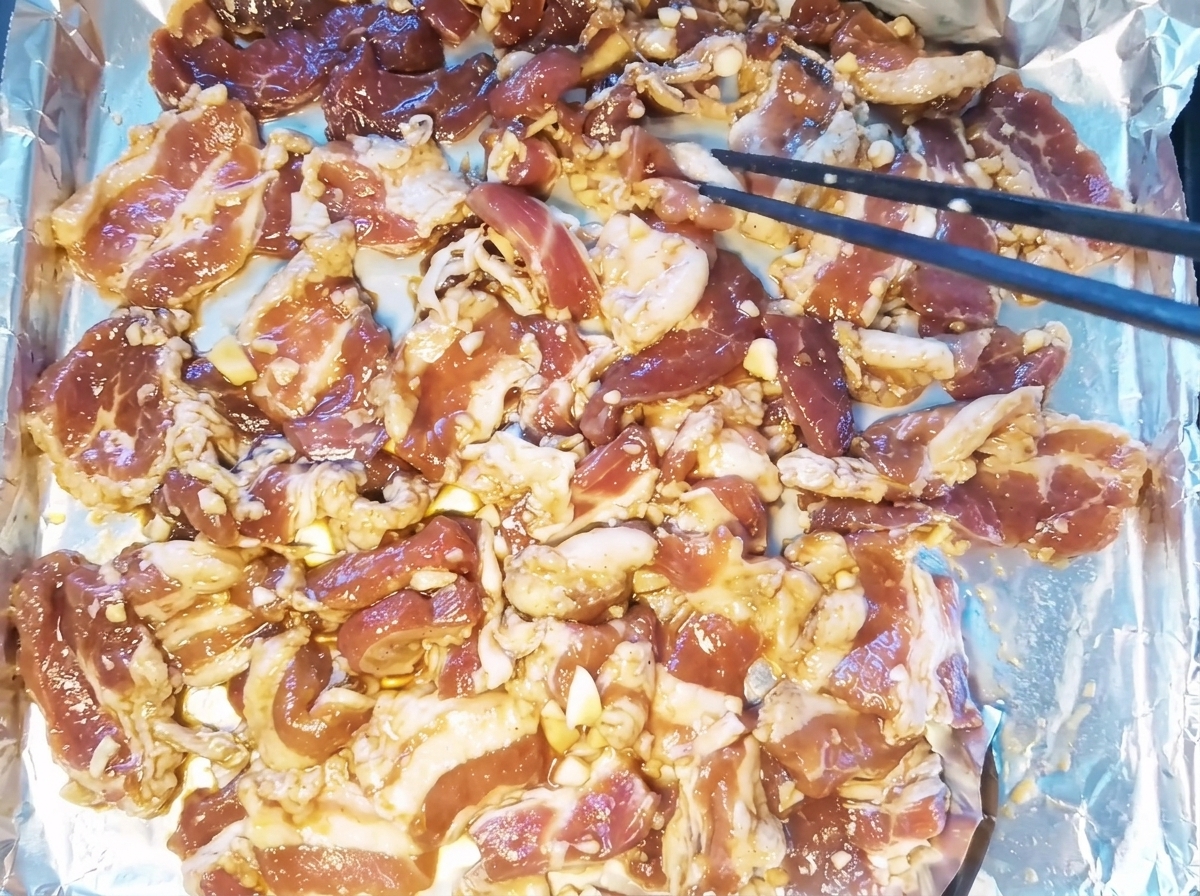 Rodajas de panceta de cerdo marinada colocadas en una sola capa sobre una bandeja para hornear forrada con papel de aluminio.