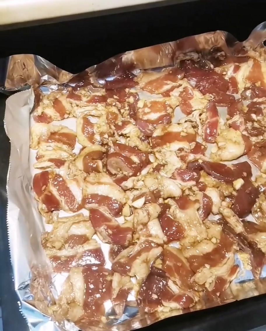 Una bandeja de hornear llena de rodajas de panceta sazonadas siendo introducida en un horno caliente.
