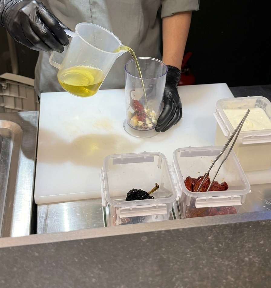 Un chef vertiendo un líquido transparente en una jarra de licuadora alta que contiene ajo y chiles.