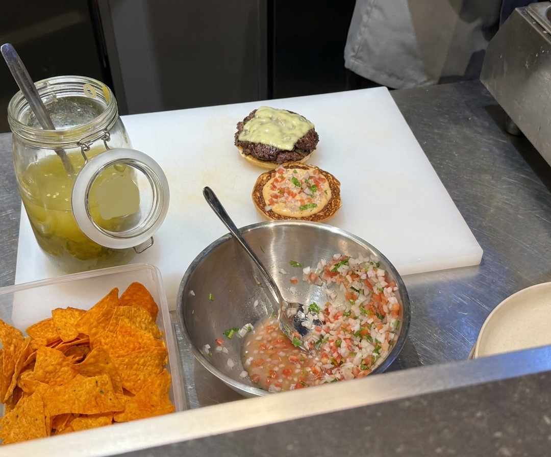 Carnes de res molida siendo aplastadas en una plancha caliente con una prensa de metal.