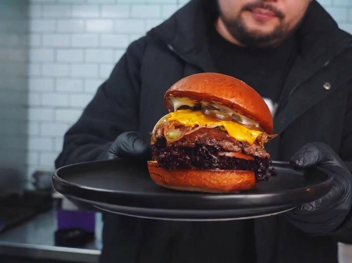 Una hamburguesa sellada en la parrilla cubierta con vegetales salteados y una rebanada de queso derritiéndose.