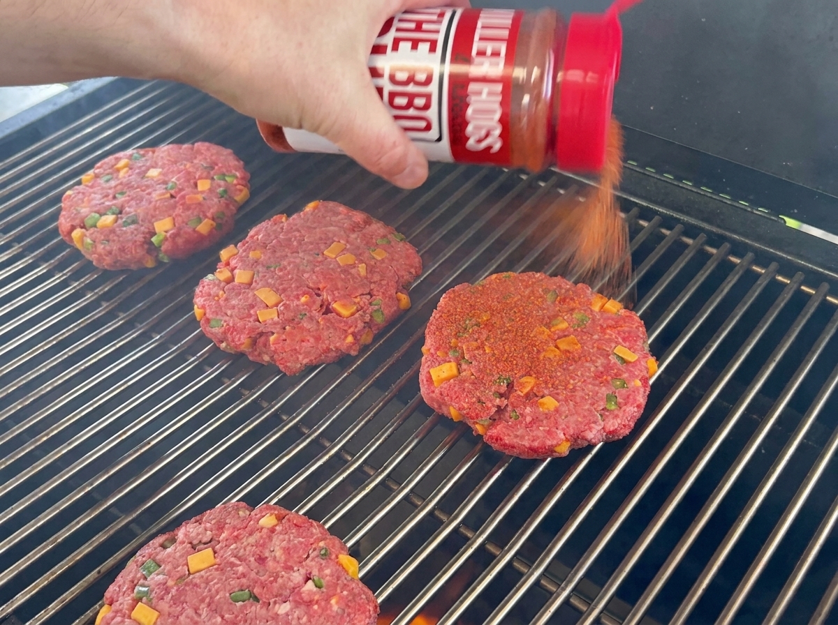 Hamburguesas de res sazonadas reposando sobre la rejilla de la parrilla.