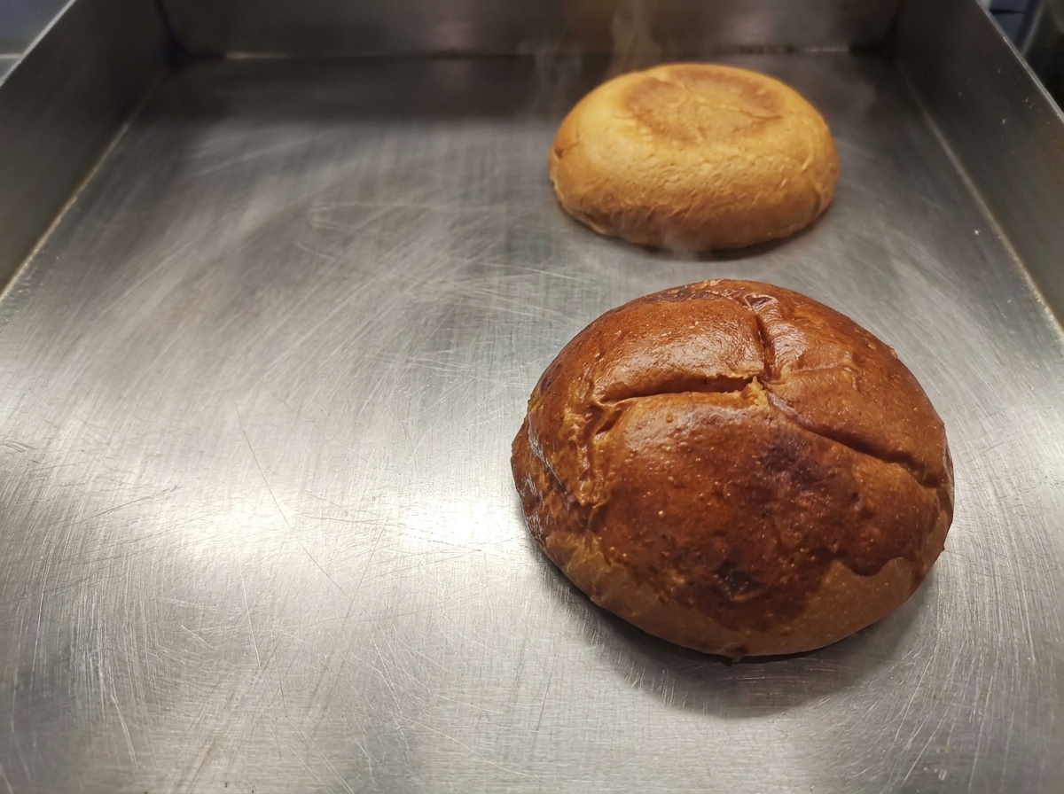 Mitades de pan de hamburguesa tostadas de color marrón dorado sobre una plancha limpia.