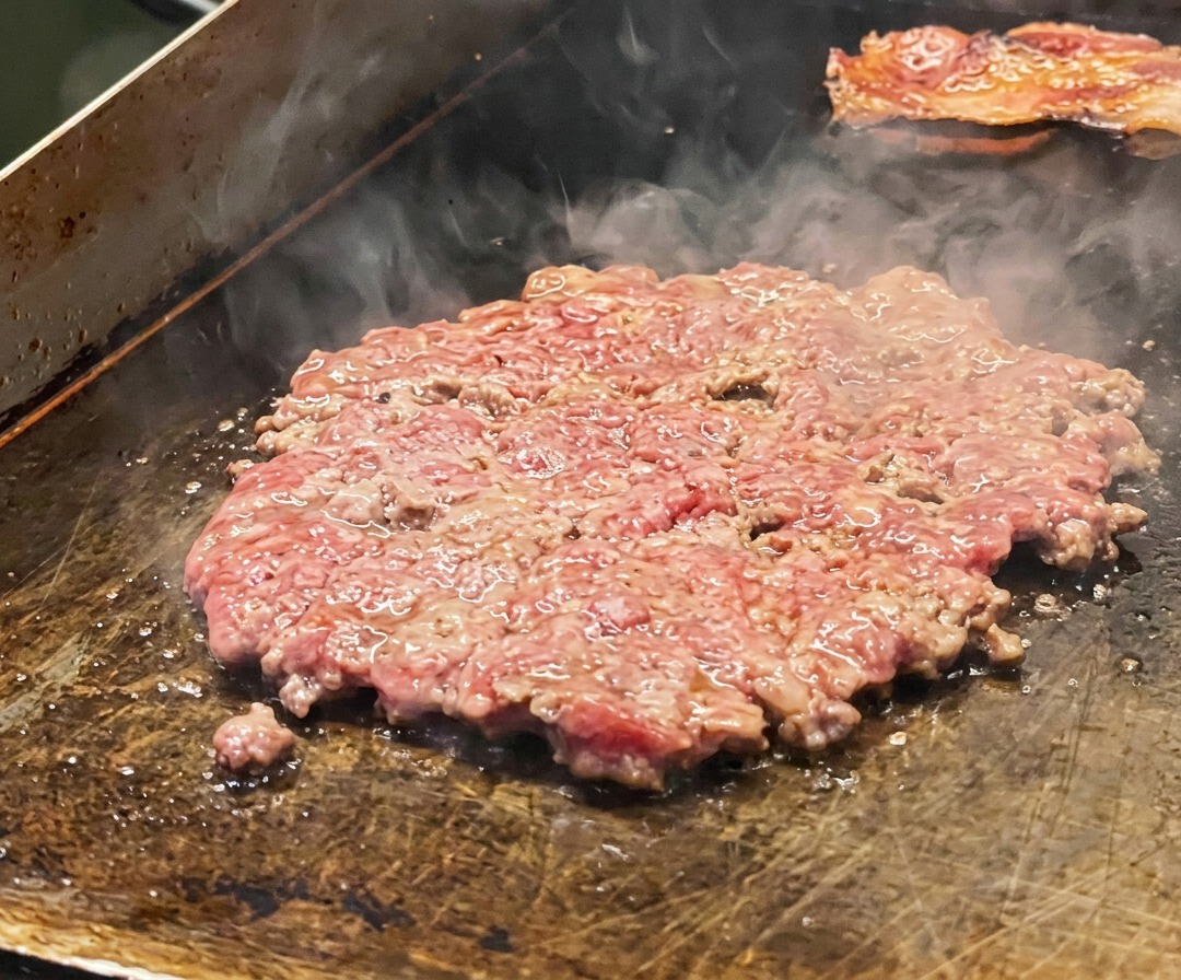 Un filete de carne fino sellándose en la plancha, sazonado con sal y cubierto con rodajas de cebolla.