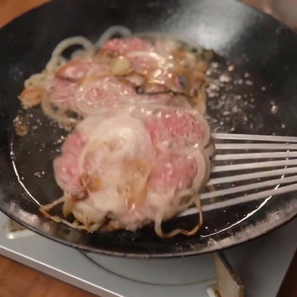 Una jugosa smash burger recién cocinada, cubierta con queso derretido, colocándose sobre un pan tostado.
