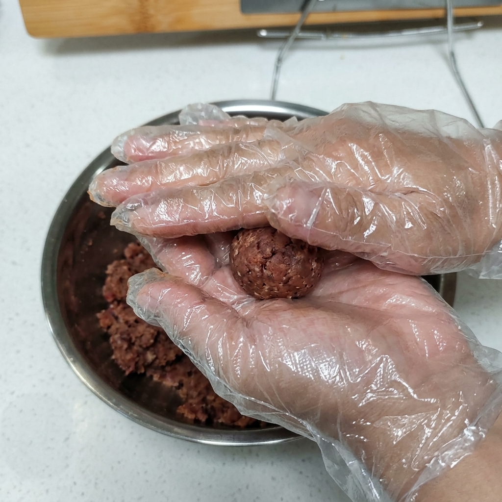 Manos enguantadas presionando una bola de carne sazonada para darle forma de hamburguesa.