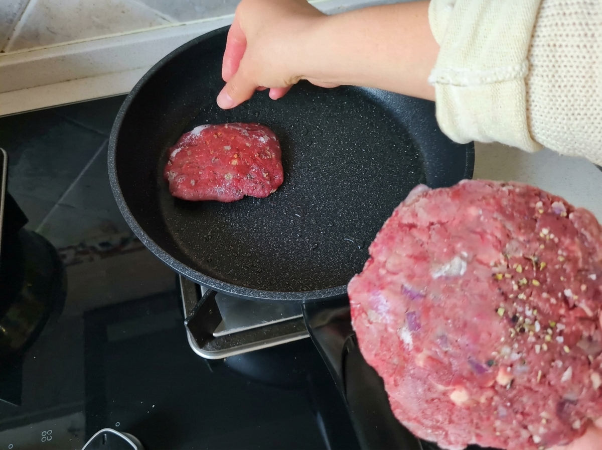 Colocando una hamburguesa cruda en una sartén antiadherente caliente.