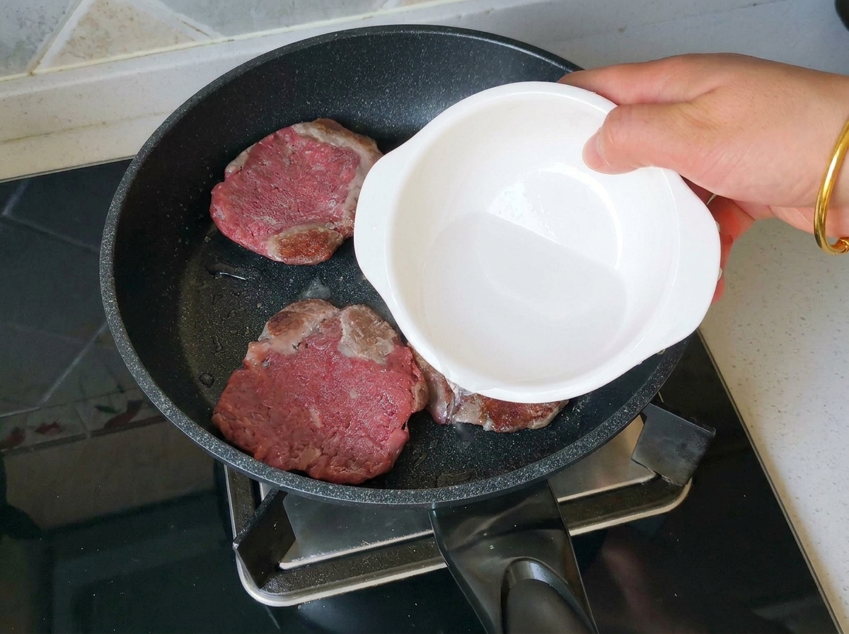 Vertiendo un chorrito de agua en la sartén con hamburguesas doradas.