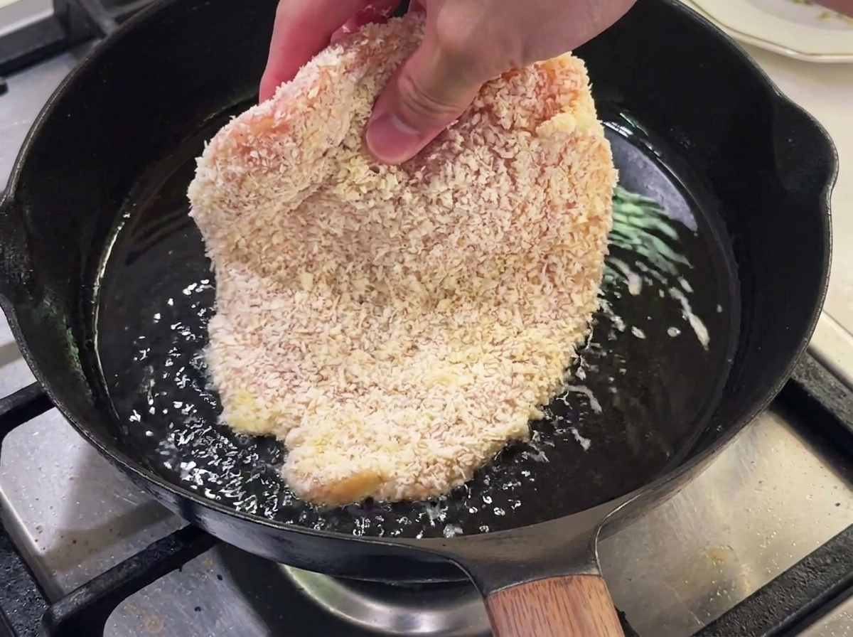Pollo empanizado friéndose en una sartén con aceite caliente.