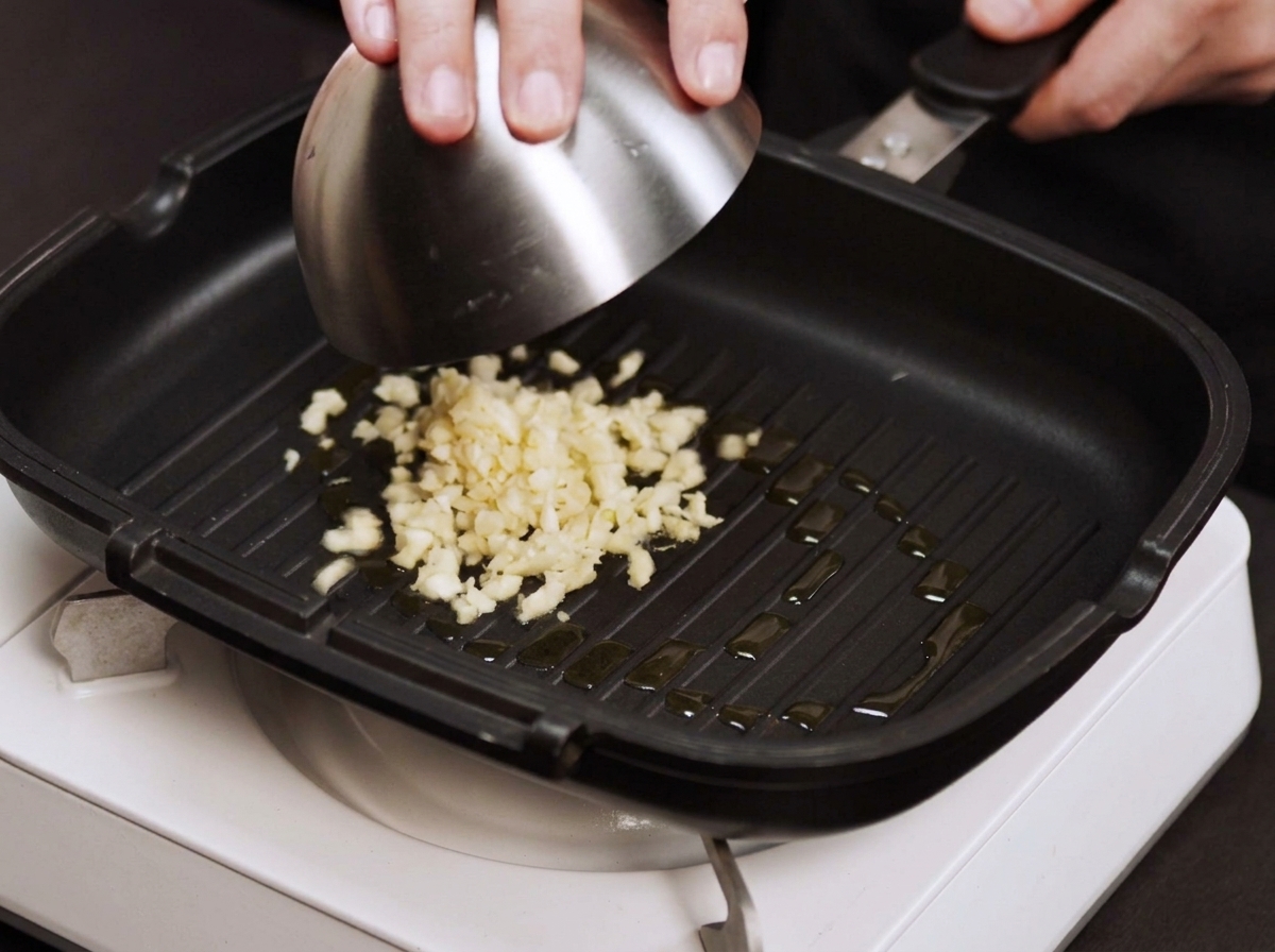 Ajos y cebollas picadas sofriéndose en una sartén caliente con poco aceite.