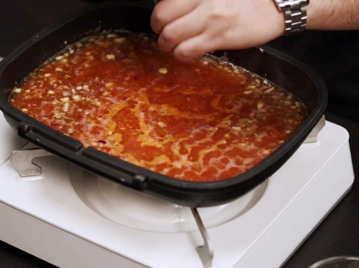 Salsa de tomate burbujeando en la sartén mientras se añade sal y pimienta.