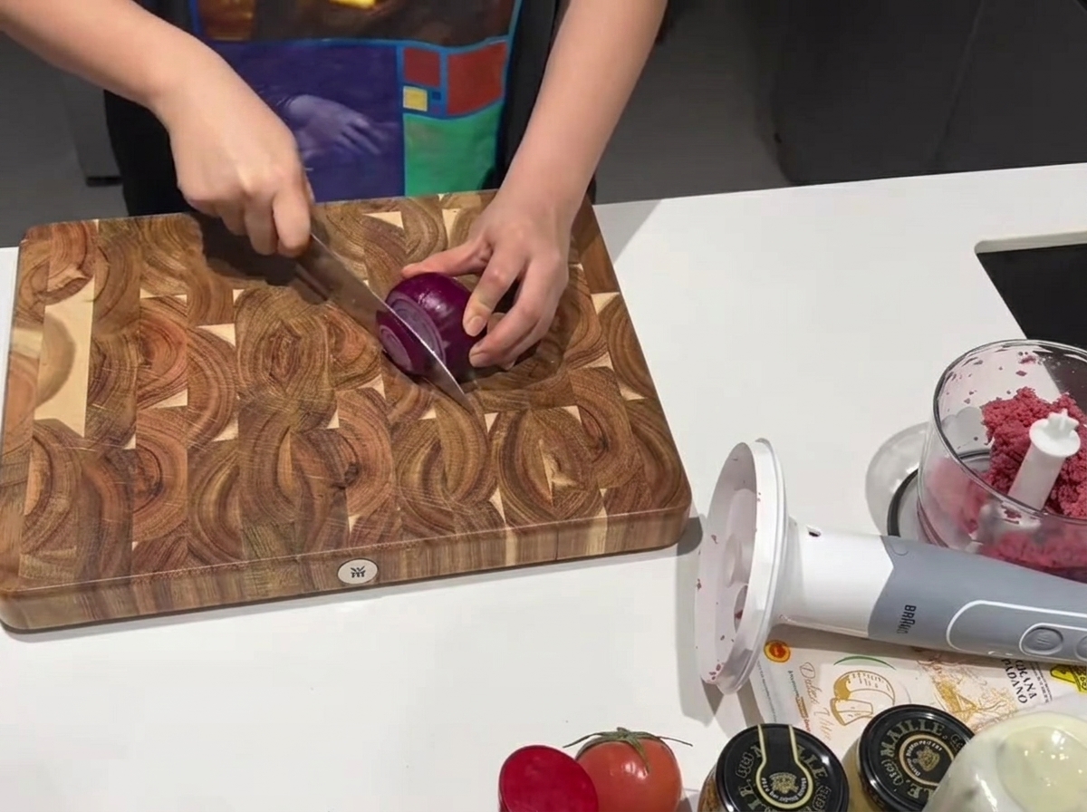 Un cuchillo de cocina afilado cortando una cebolla morada fresca sobre una tabla de madera.