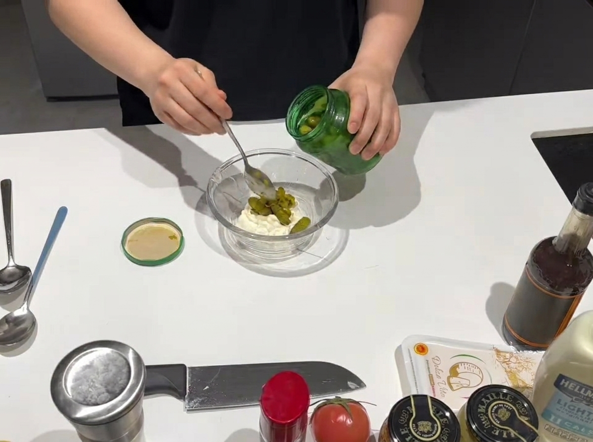 Una cucharada de relish dulce agregándose a un bol con mayonesa cremosa.