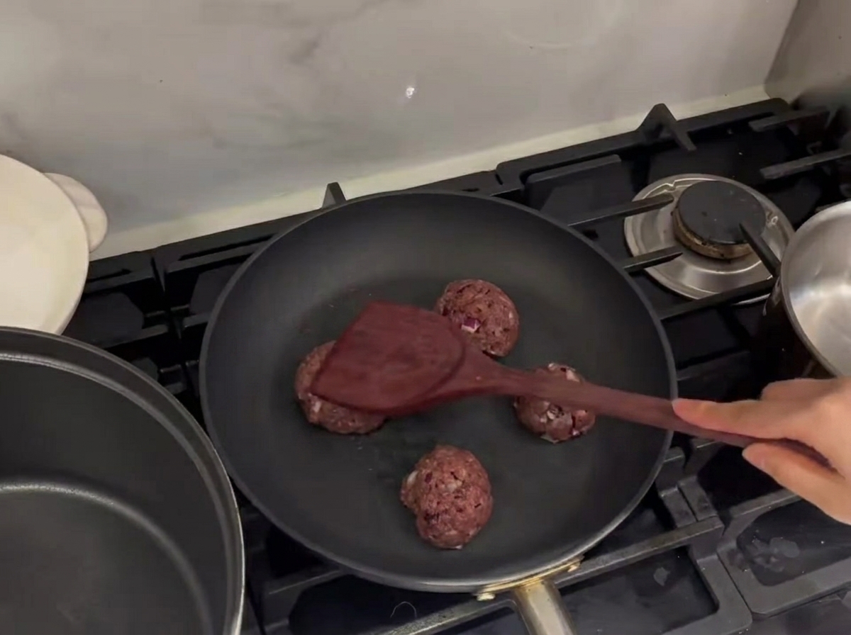 Albóndigas de carne aplastándose en una sartén caliente con una espátula de metal.