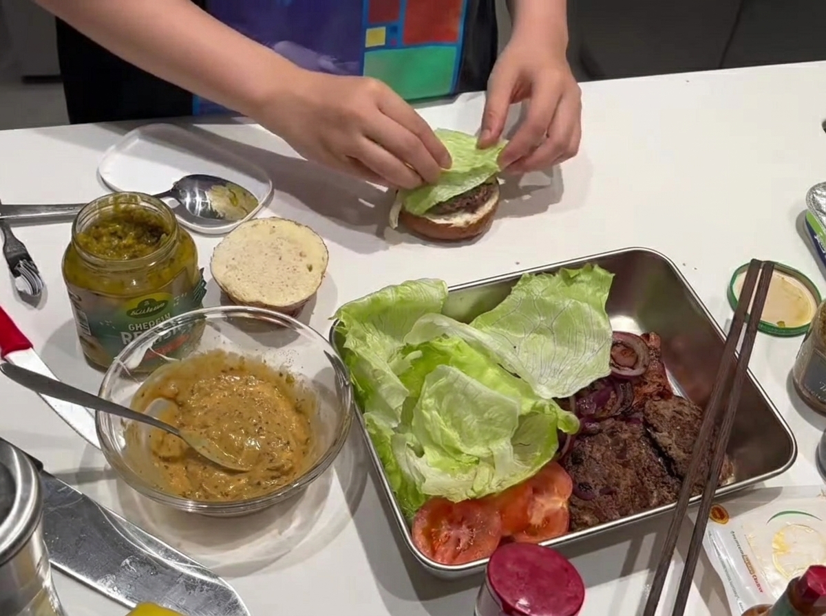 Una hoja de lechuga fresca colocándose sobre la carne de la hamburguesa.