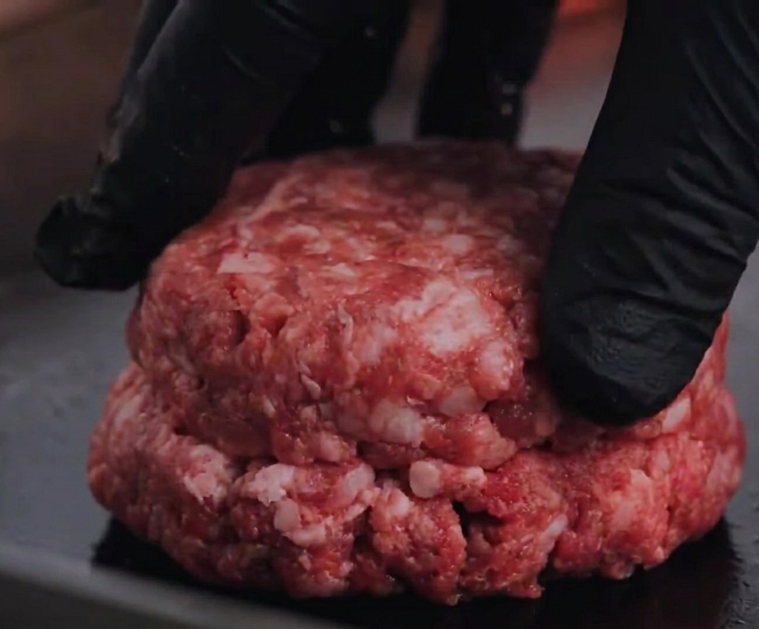 Una hamburguesa de carne Angus cruda siendo presionada contra una parrilla caliente.