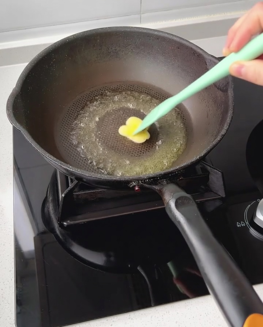 Un trozo pequeño de mantequilla derritiéndose en una sartén antiadherente siendo esparcido con una espátula.