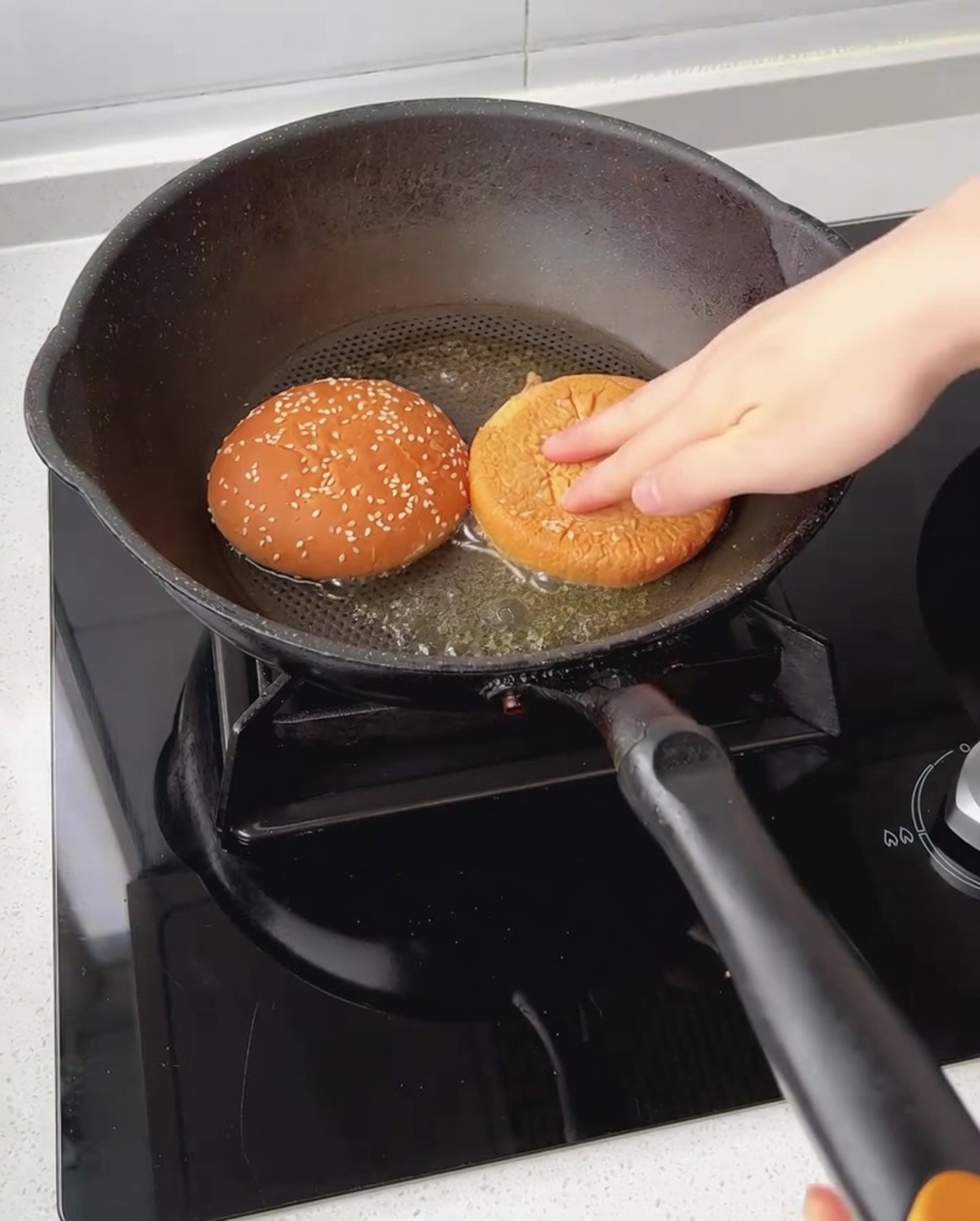 Mitades de pan de hamburguesa tostándose boca abajo en una sartén con mantequilla derretida.