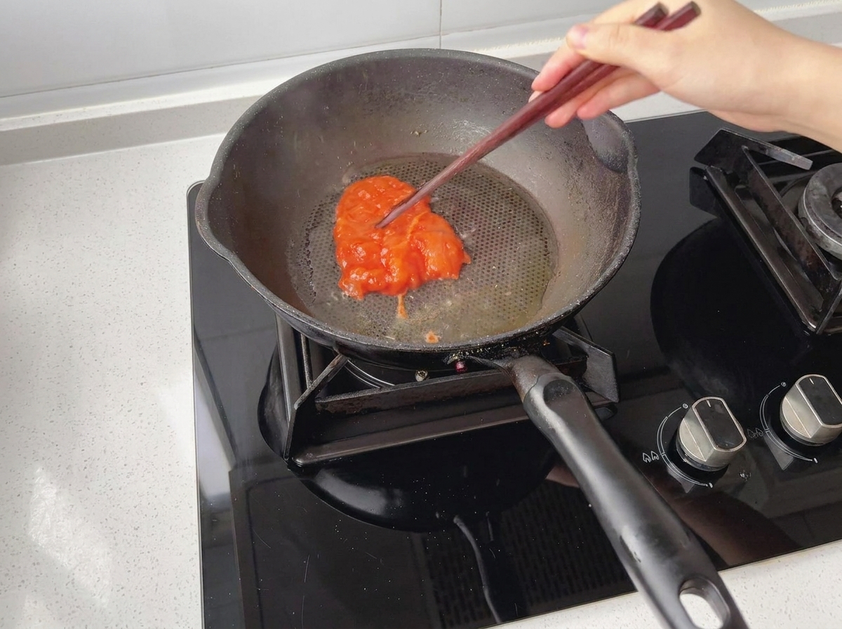Trozo de pollo marinado siendo colocado en una sartén precalentada y aceitada.