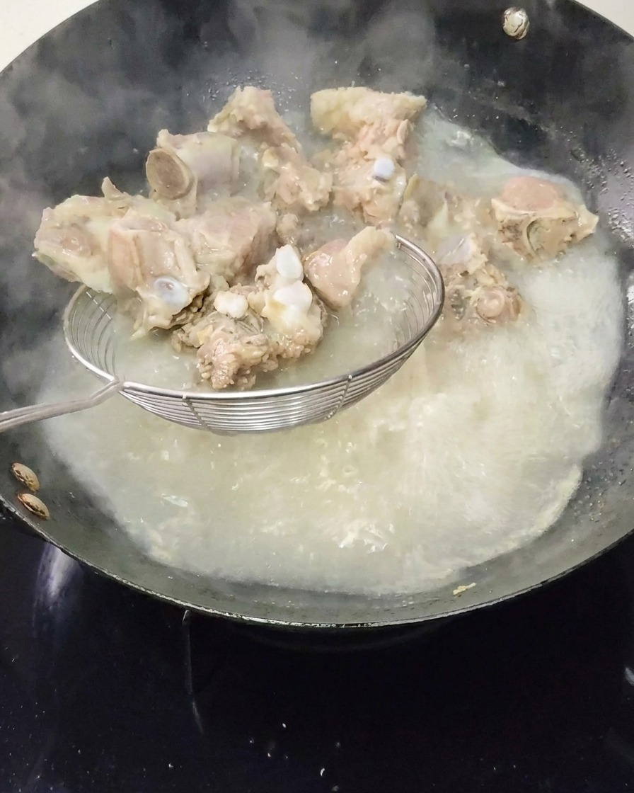 Costillas de cerdo blanqueadas siendo retiradas del agua hirviendo con una espumadera.