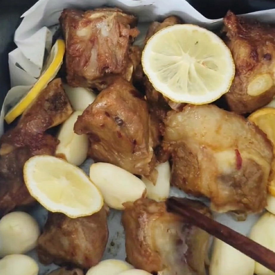 Costillas de cerdo siendo volteadas en la freidora de aire y pinceladas con un glaseado de miel, con dientes de ajo tostados visibles.
