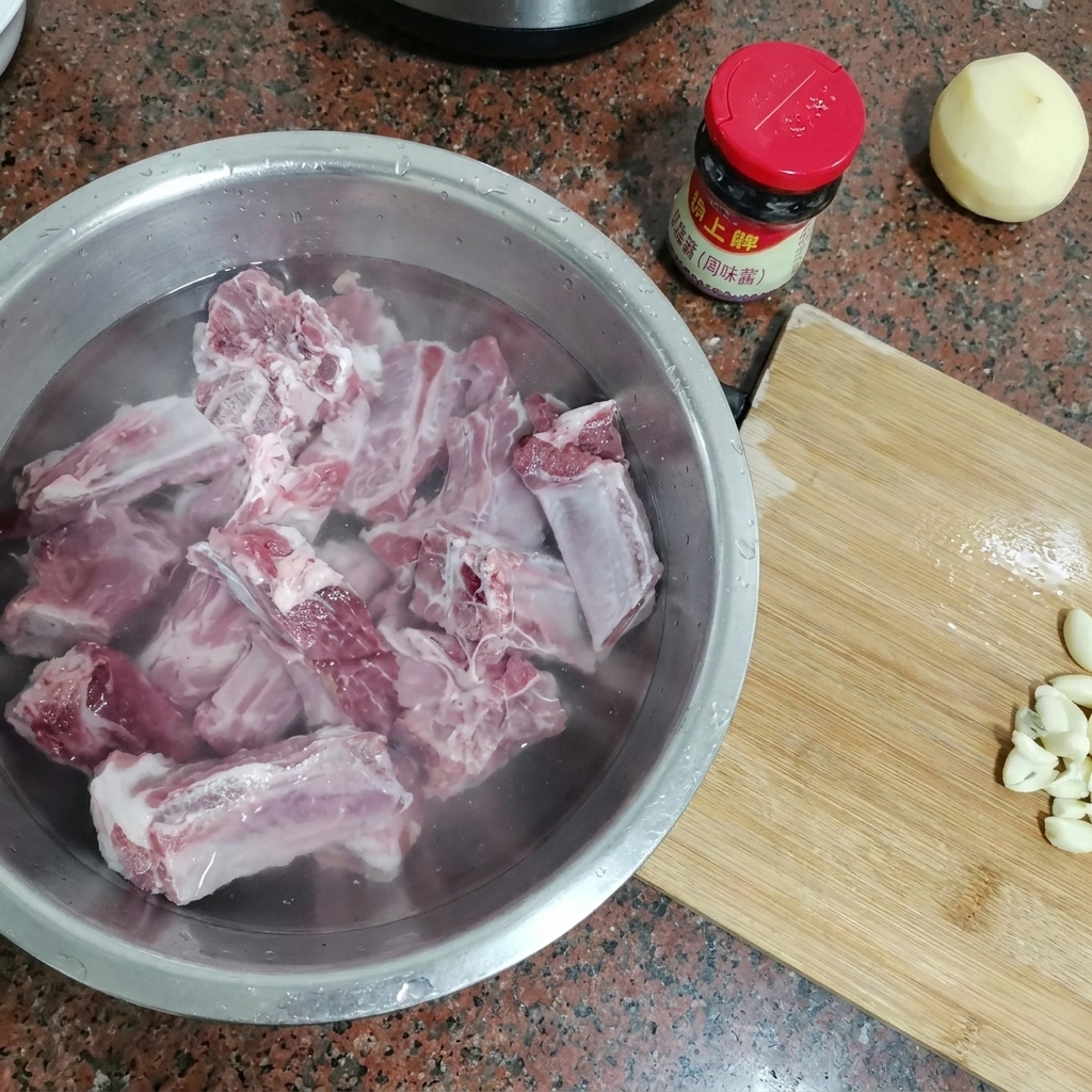 Costillas de cerdo crudas sumergidas en un bol de metal grande lleno de agua fría.