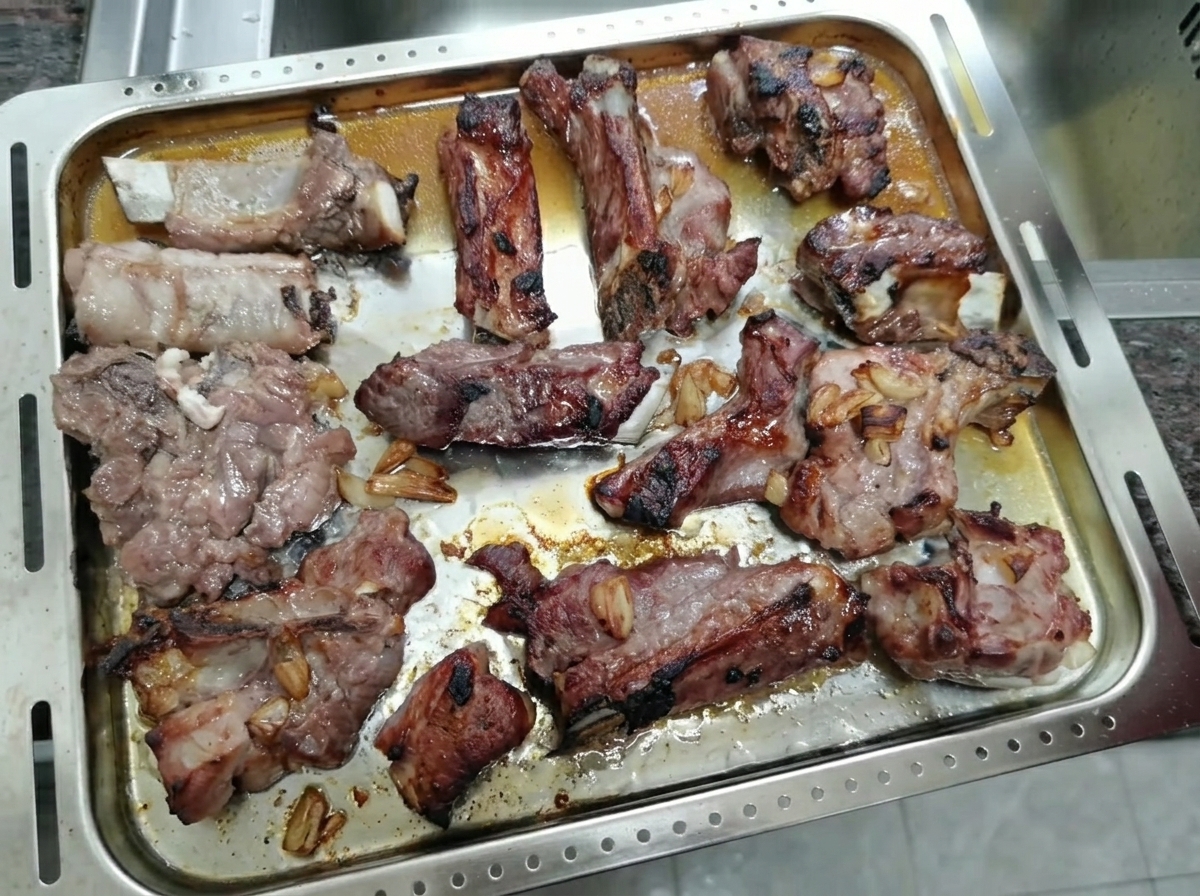 Costillas de cerdo asadas y caramelizadas reposando en una bandeja de metal.