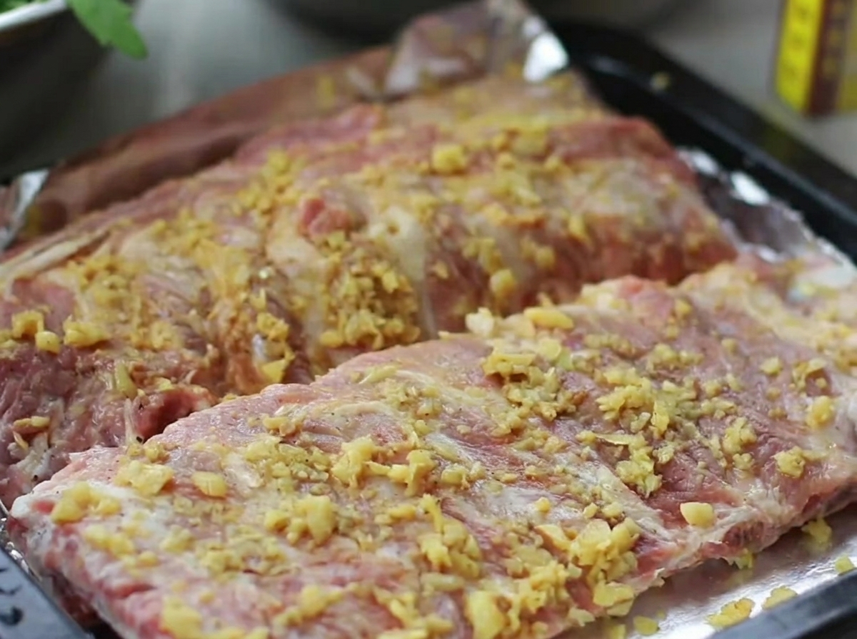 Una bandeja de horno con costillas de cerdo sazonadas, herméticamente envueltas con una capa de papel aluminio brillante.