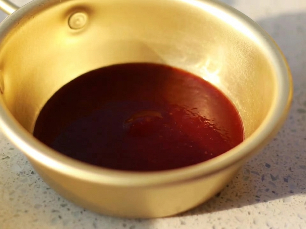Un pequeño cuenco de metal que contiene una mezcla suave de salsa barbacoa, salsa de ostra, mostaza, miel y salsa de soja clara.