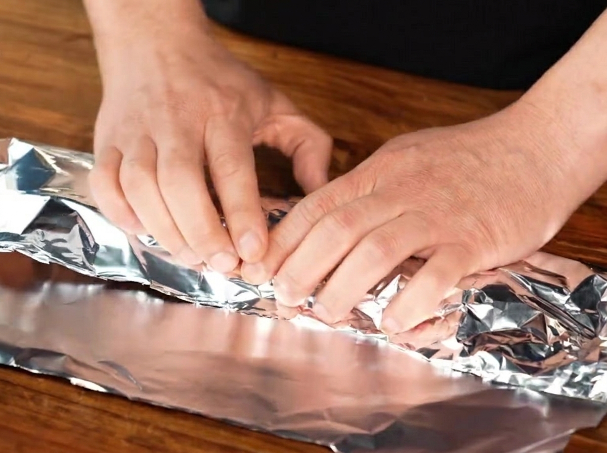 Costillas de cerdo sazonadas siendo envueltas herméticamente dentro de una hoja de papel aluminio.