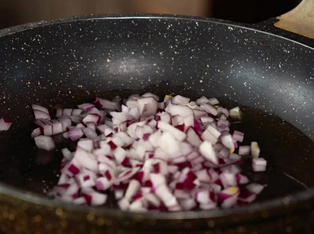 Cebolla morada picada, ajo picado y jengibre cocinándose en una sartén con aceite.