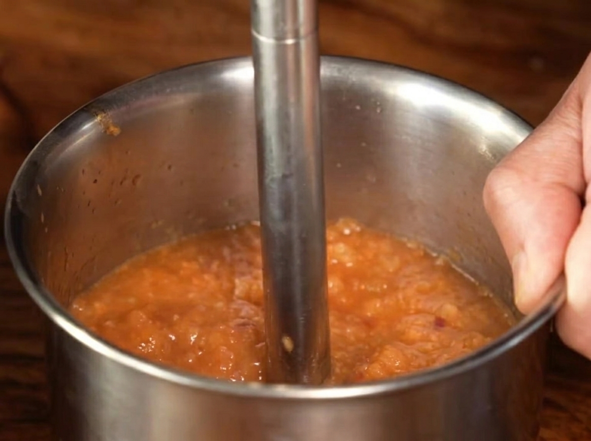 Una licuadora de mano metálica procesando la mezcla de salsa cocida hasta convertirla en un puré suave.