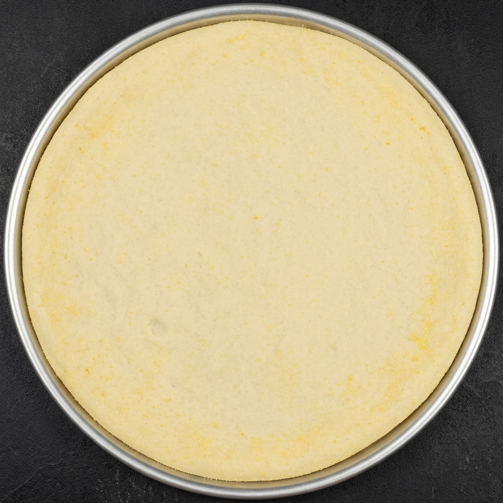 Un círculo de masa de pizza dentro de un molde de metal, con cortes radiales a lo largo del borde exterior.