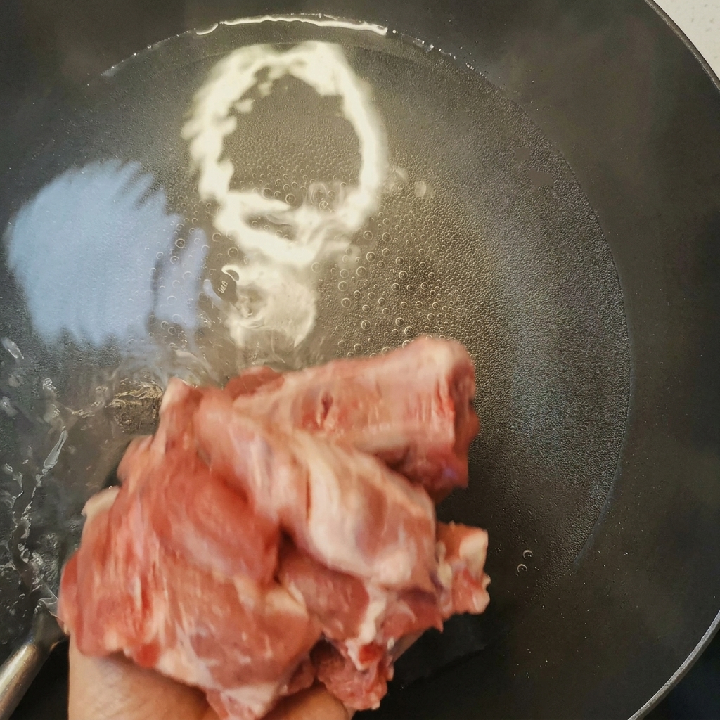 Costillas de cerdo siendo blanqueadas en una olla con agua hirviendo y vino de cocina, mostrando la espuma que sube a la superficie.