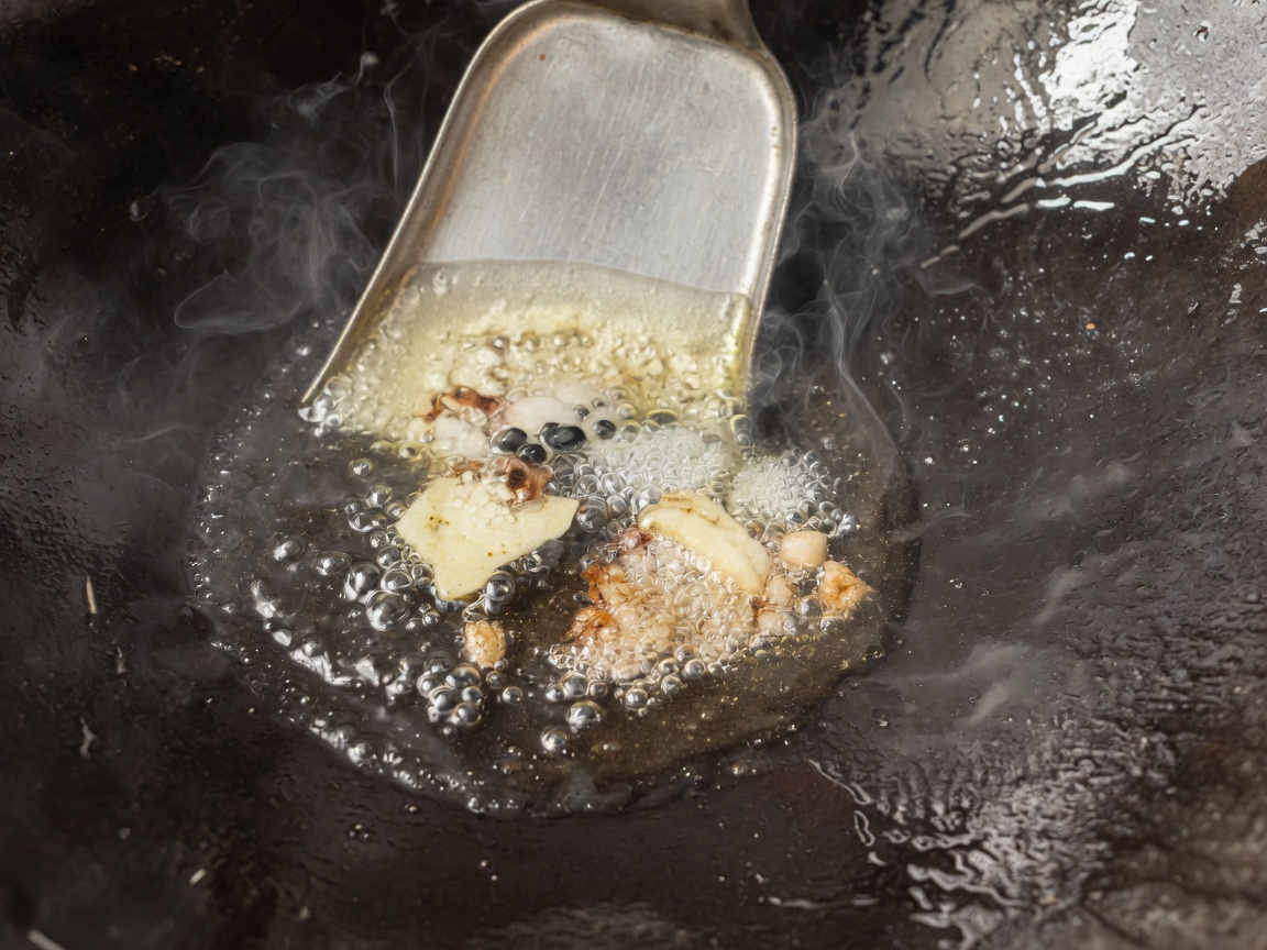 Aromáticos y especias chisporroteando en aceite caliente dentro de un wok sazonado.