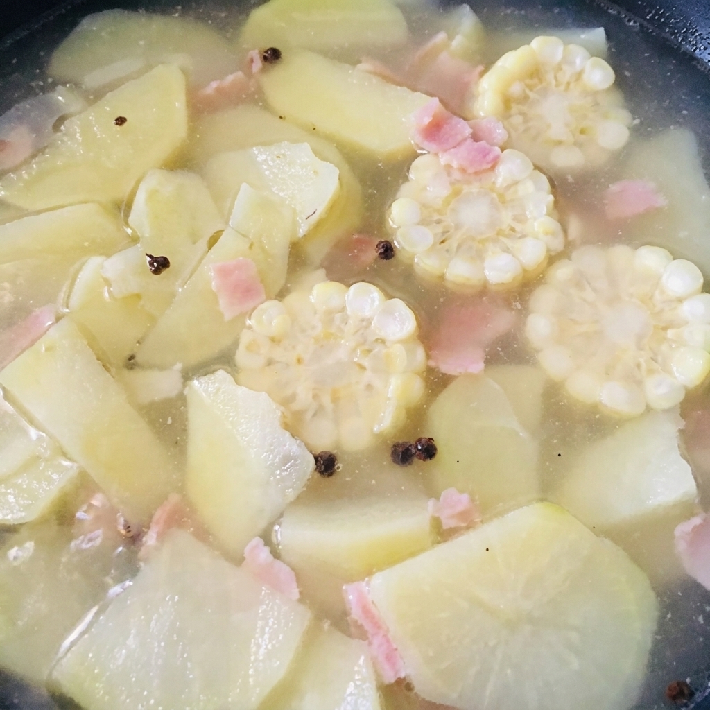 Carne de almeja sin concha siendo añadida a una olla con sopa de maíz y brotes de bambú hirviendo a fuego lento.