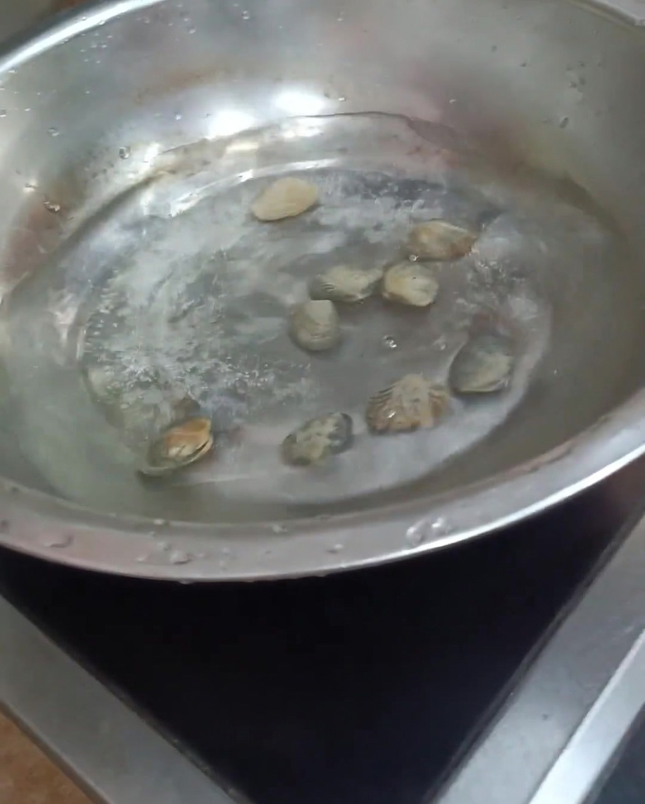 Almejas cocinándose en una olla con agua hirviendo, con algunas conchas empezando a abrirse.