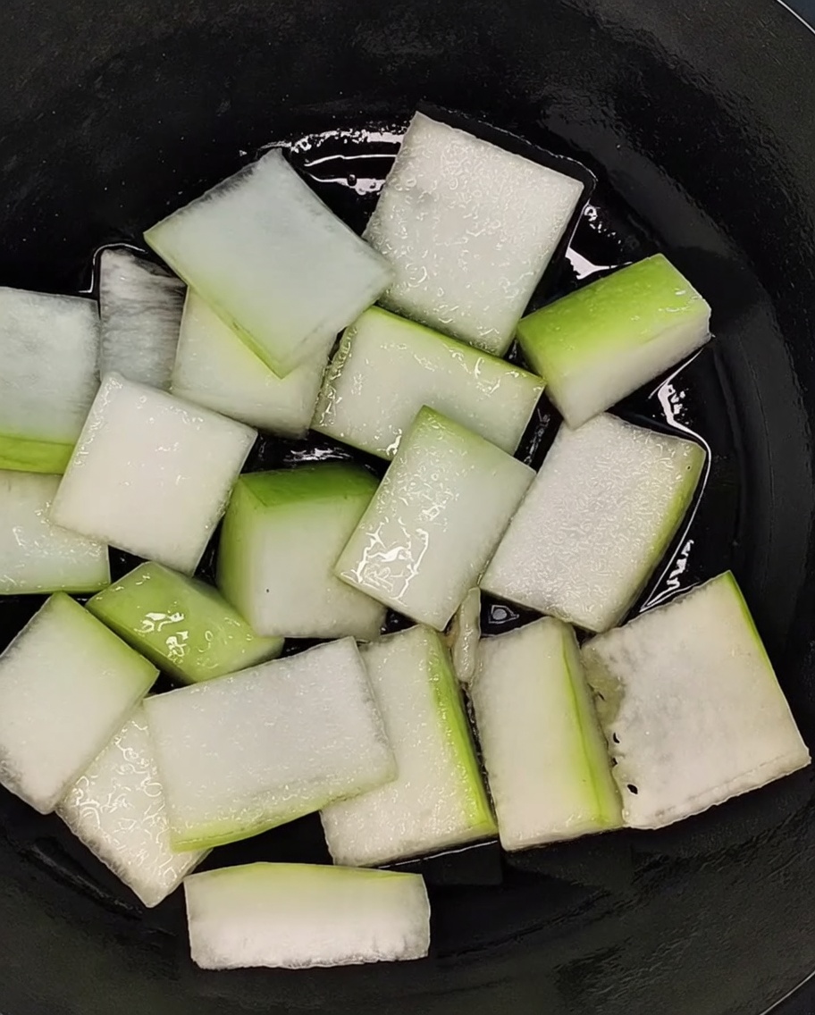 Trozos de melón de invierno cortados en rodajas, dispuestos uniformemente para cubrir el fondo de una olla negra.