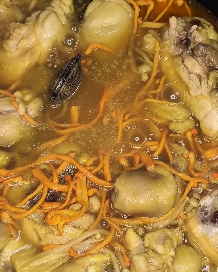 Almejas frescas agregándose a la olla hirviendo a fuego lento, descansando sobre el pollo y las verduras cocidas.