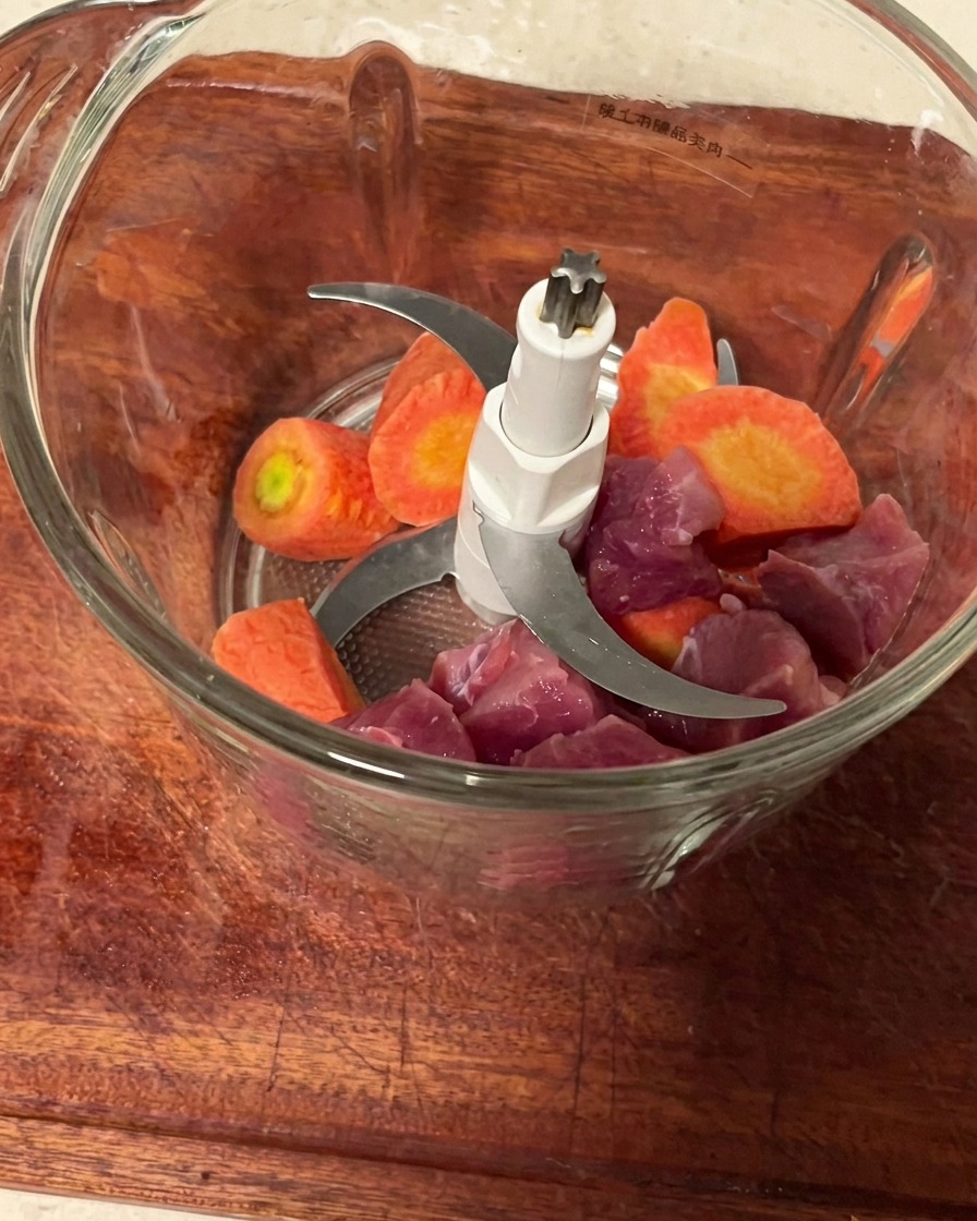 Trozos de cerdo y zanahoria dentro de un vaso de picadora limpio, listos para ser procesados.