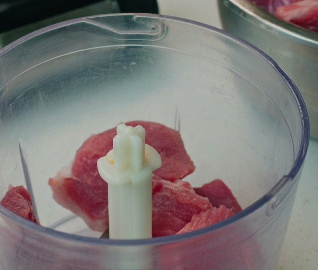 Trozos de cerdo picado dentro del vaso de un procesador de alimentos.