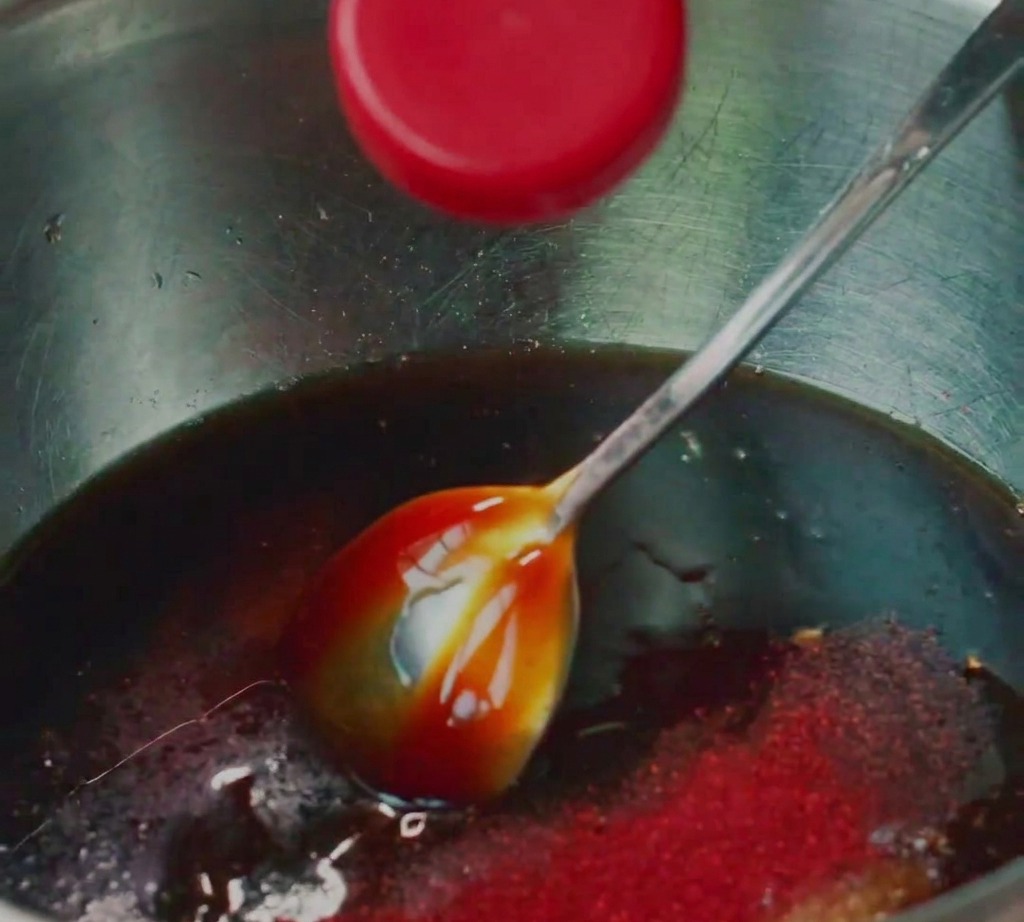 Carne de cerdo picada mezclándose con diversos condimentos líquidos en un cuenco de acero inoxidable.
