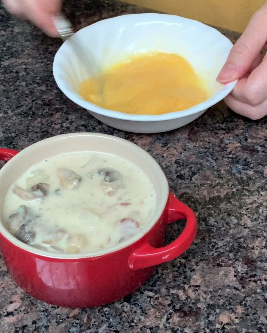 Una hoja redonda de hojaldre siendo colocada para cubrir un pequeño cuenco de sopa rojo.