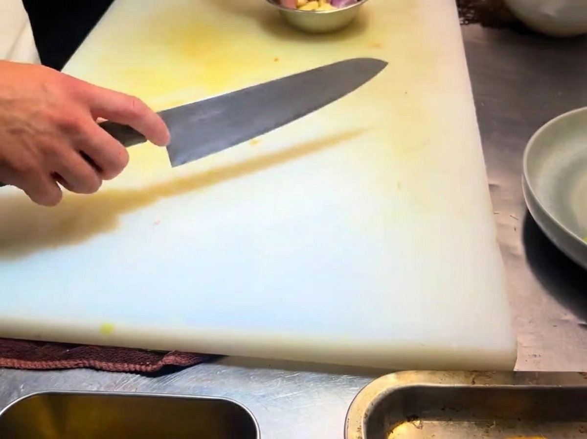 Dientes de ajo cortados en láminas finas sobre una tabla de cortar blanca.